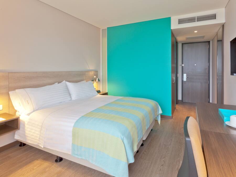 Una habitación de hotel con una cama, mesita de noche, lámpara y una cafetera sobre una mesa de madera.