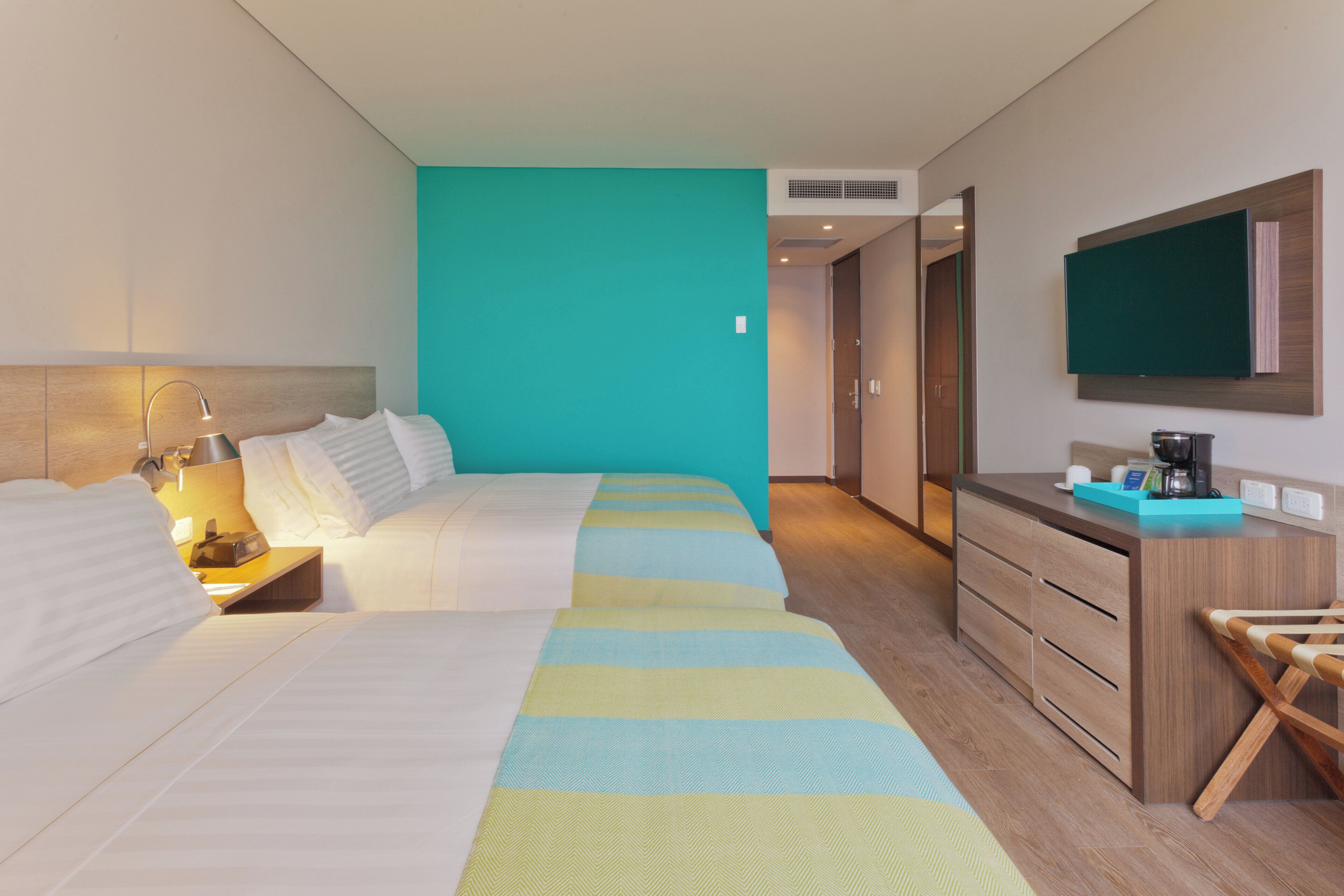 Habitación de hotel con cama, mesita de noche, lámpara y televisor montado en la pared.