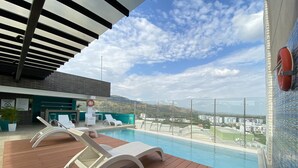 Área de piscina en la azotea con sillones, un flotador salvavidas y vistas a la ciudad y montañas.
