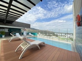 Área de piscina en la azotea con sillones, un flotador salvavidas y vistas a la ciudad y montañas.