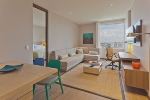 Una habitación de hotel moderna con sofá, mesa de comedor, silla, mesa de centro y televisor montado en la pared.