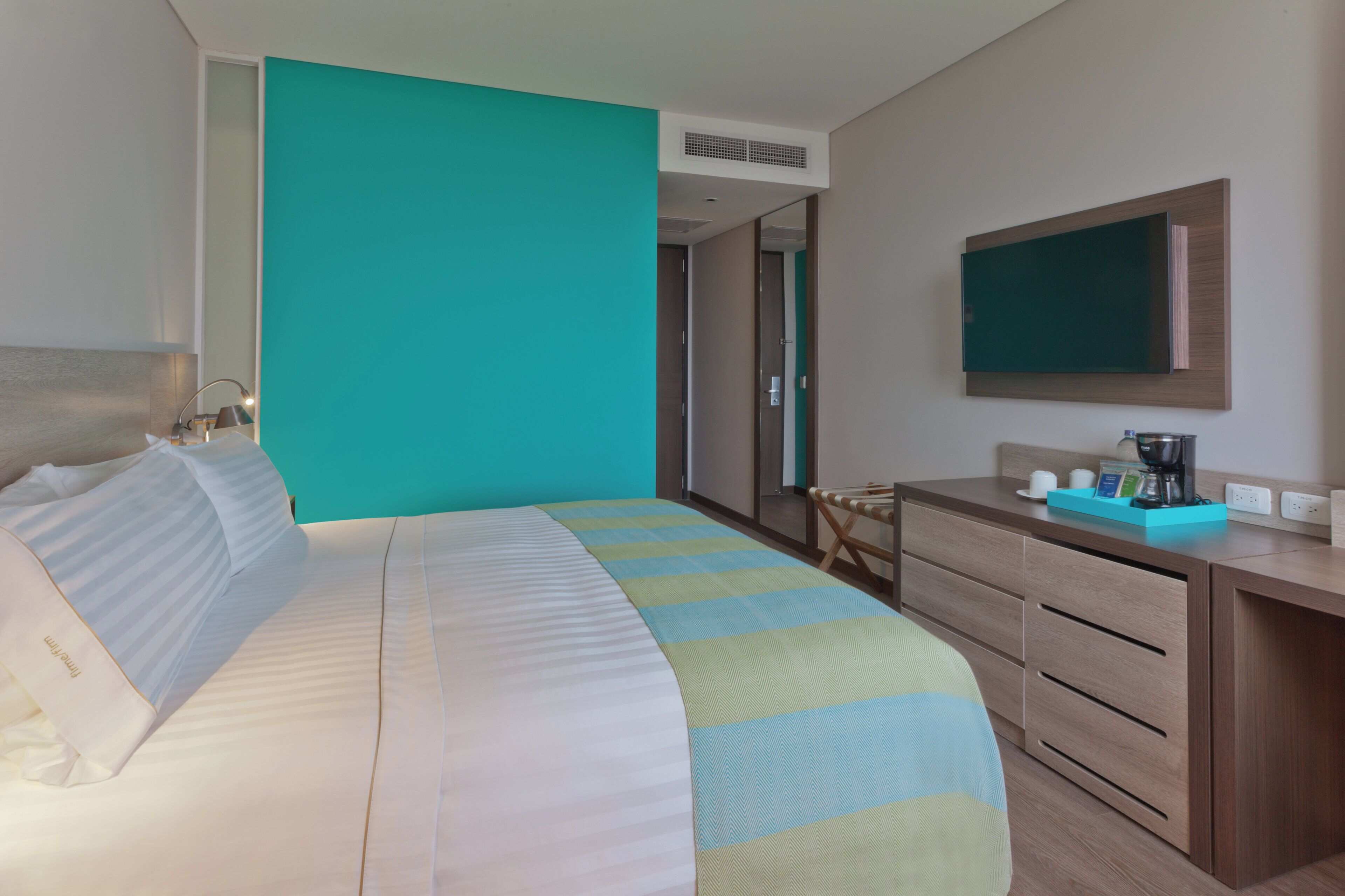 A hotel room with a bed, a desk, a mirror, and a window.