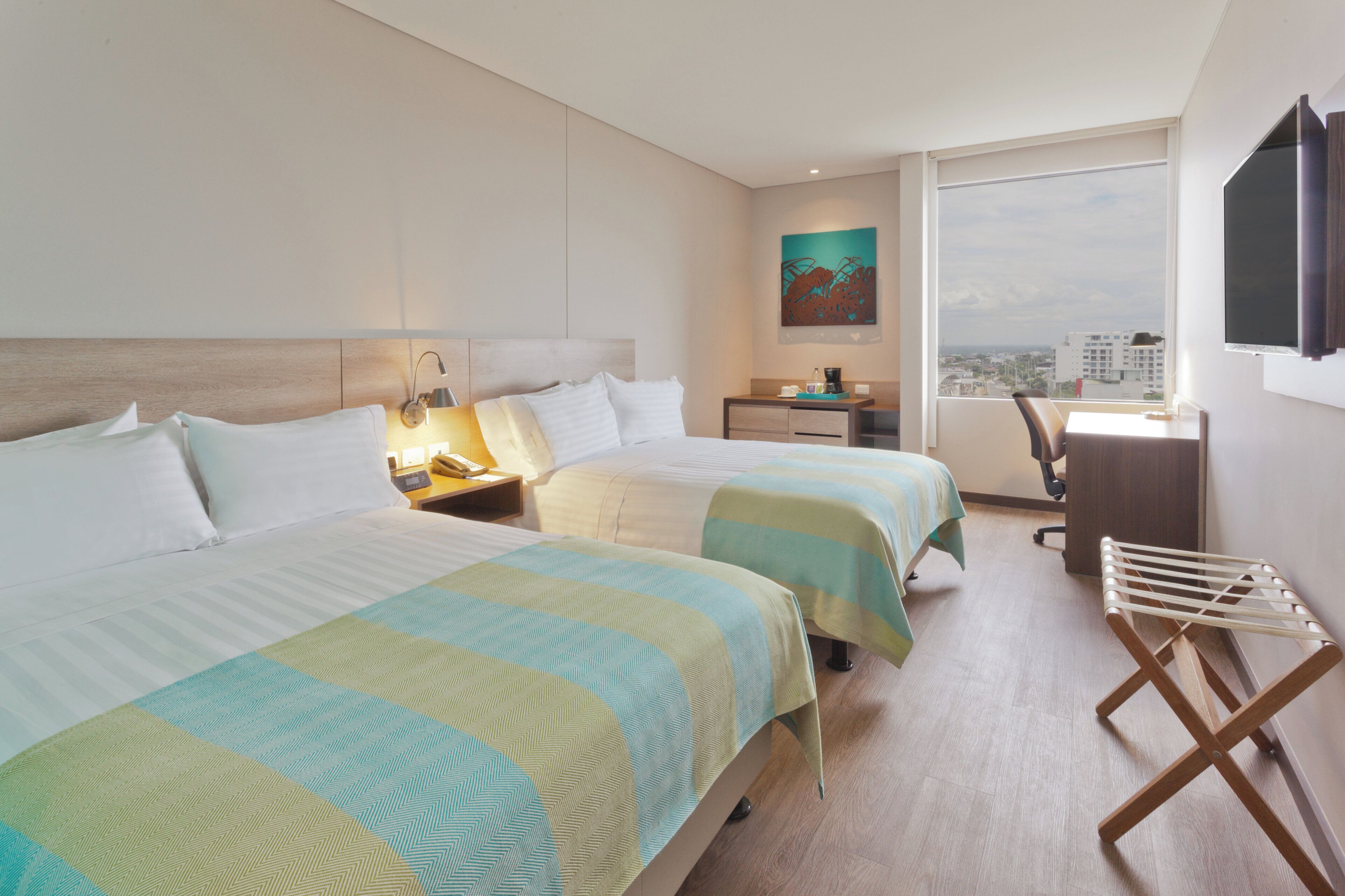 Habitación de hotel con dos camas, un escritorio, una silla, un televisor y una ventana con vista a la ciudad.