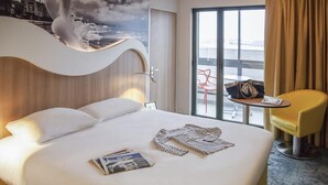 Habitación de hotel con cama, una silla, una mesa y vista al exterior.