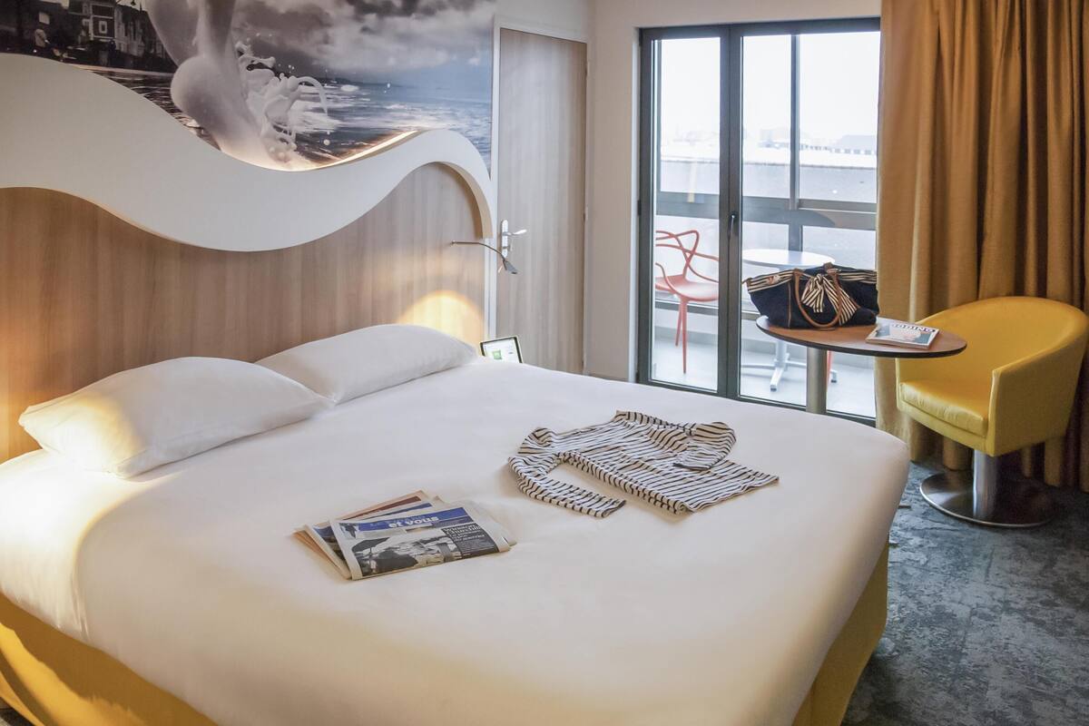 Habitación de hotel con una cama grande, una mesita con una silla y vistas amplias por una ventana.