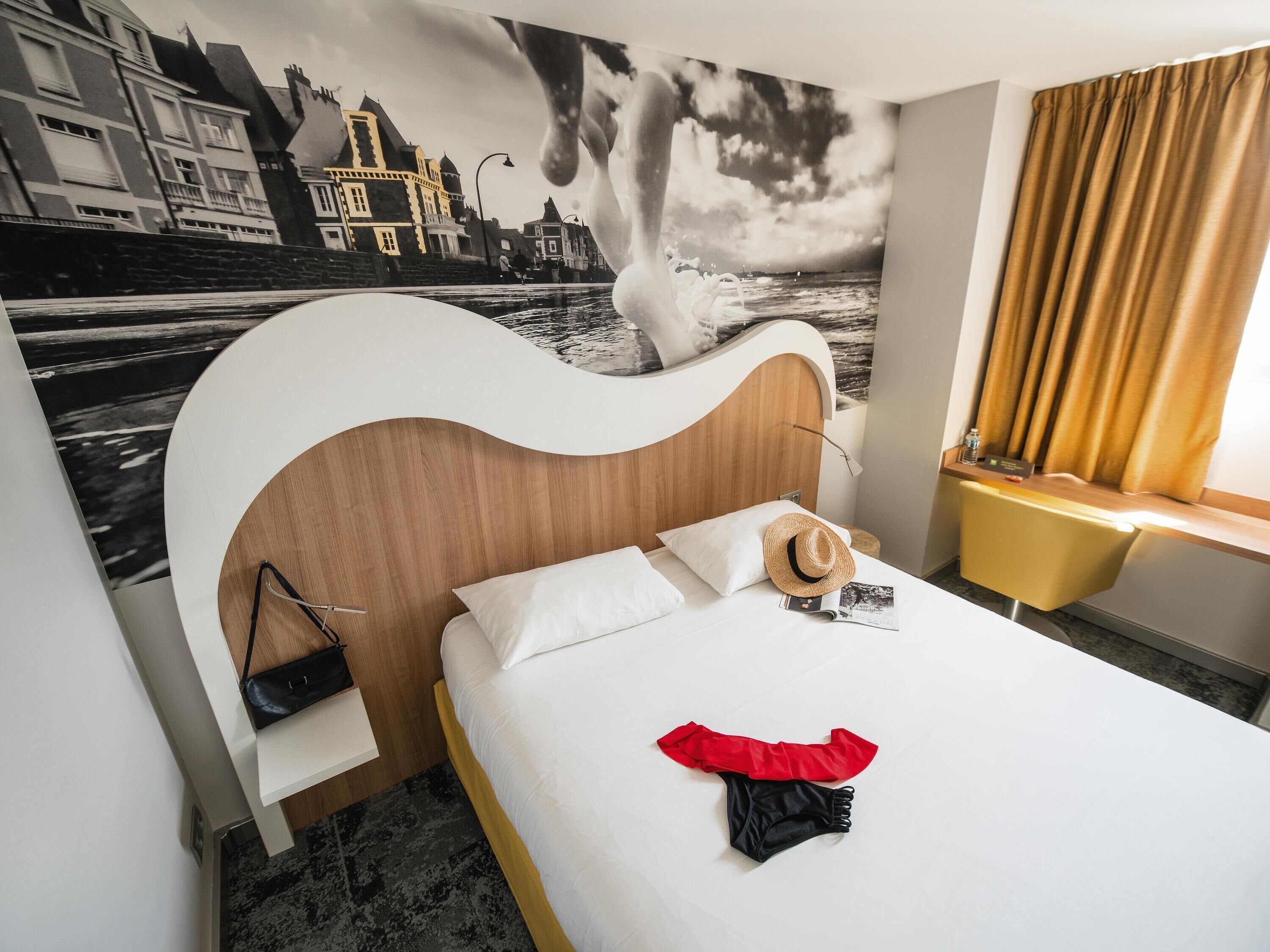 Una habitación de hotel con una cama, un mural en la pared, un escritorio y una ventana con cortinas.