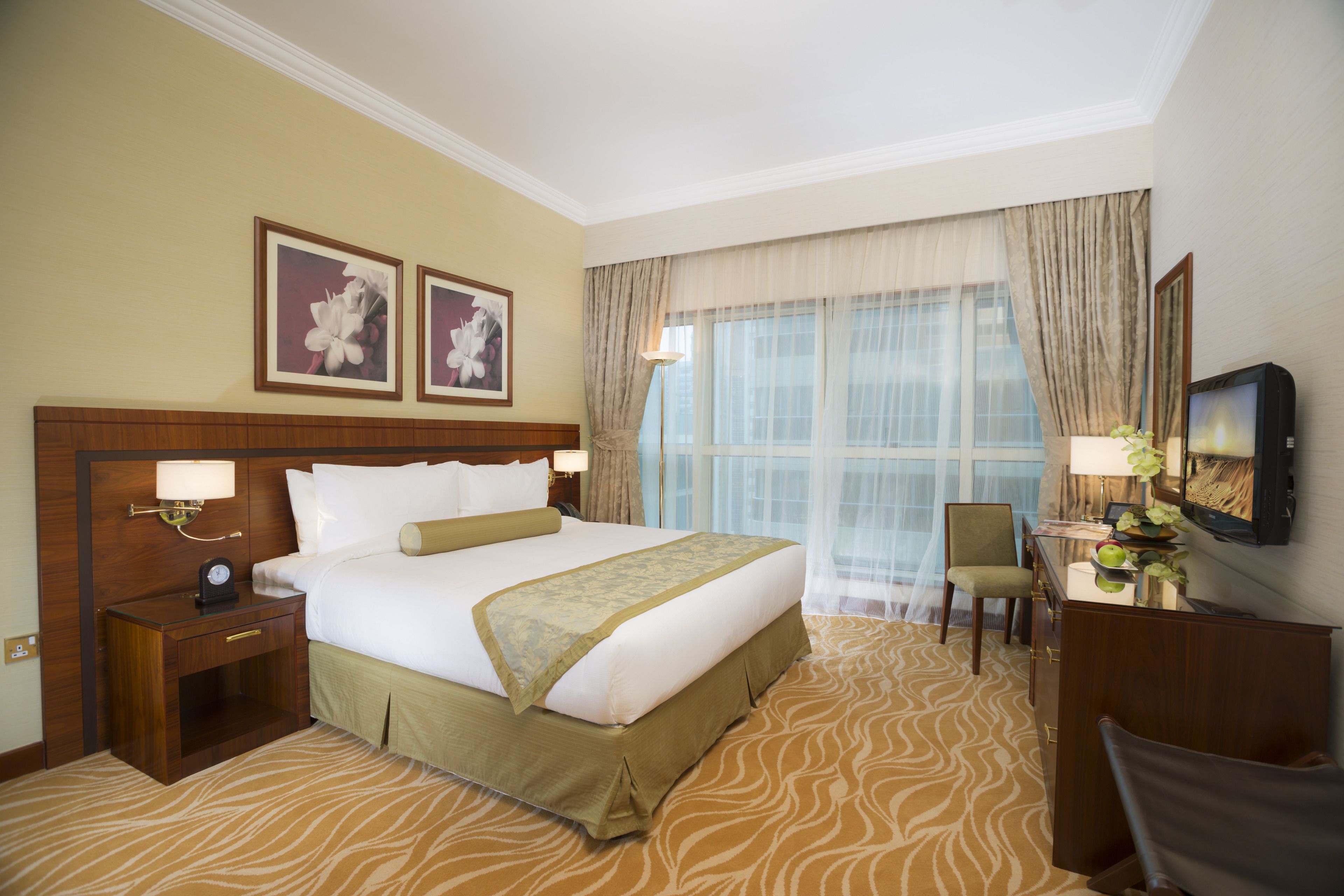 Quarto de hotel com uma cama grande, uma escrivaninha com cadeira, televisão e duas imagens emolduradas na parede.