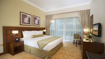 Quarto de hotel com uma cama grande, uma escrivaninha com cadeira, televisão e duas imagens emolduradas na parede.