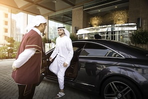 A man in traditional attire exiting a luxury car near a modern building with reflective glass windows and a chandelier. - Majlis Grand Mercure Residence Abu Dhabi (Abu Dhabi)