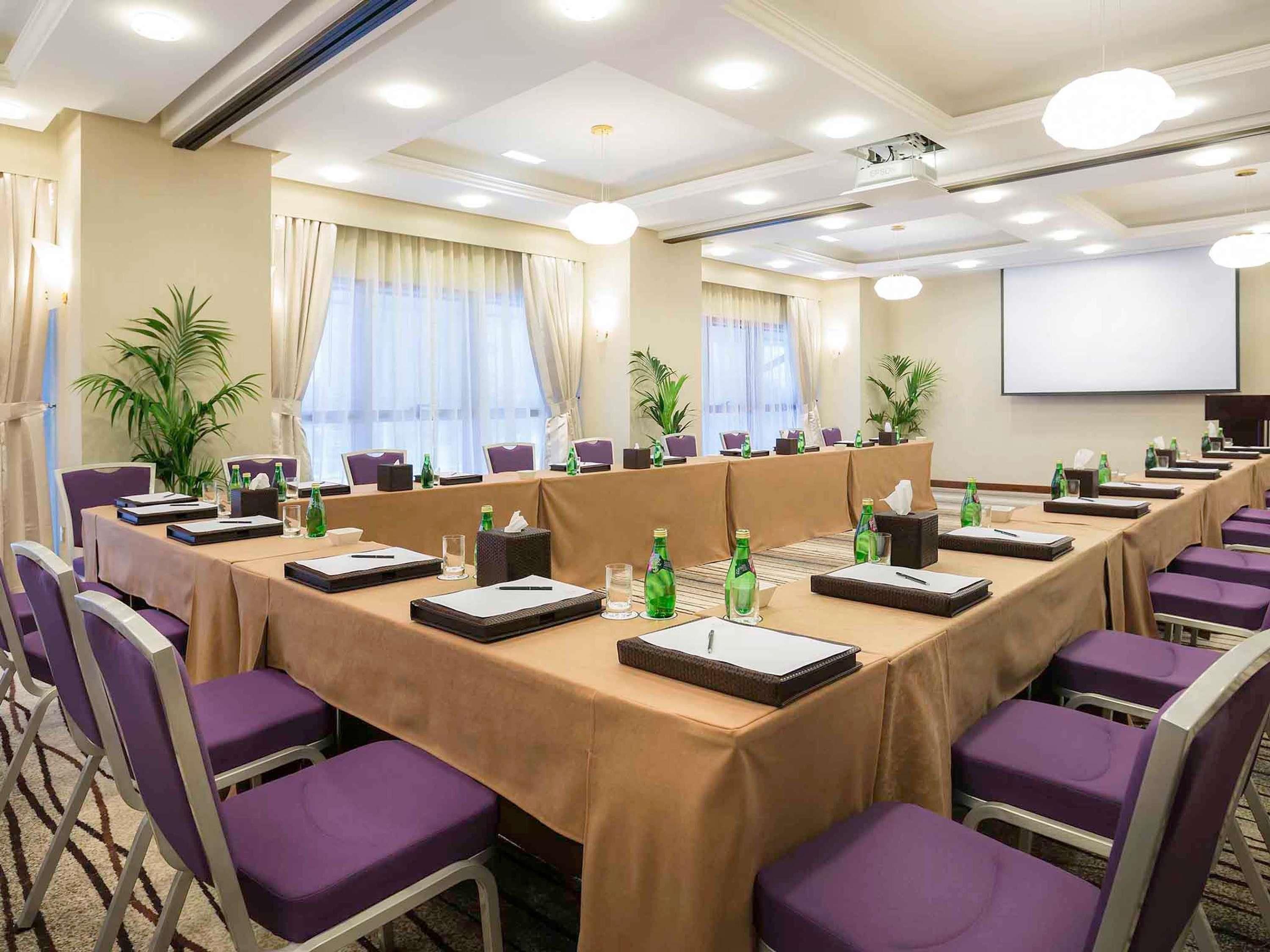 A conference room with a long table, chairs, and a projector screen.