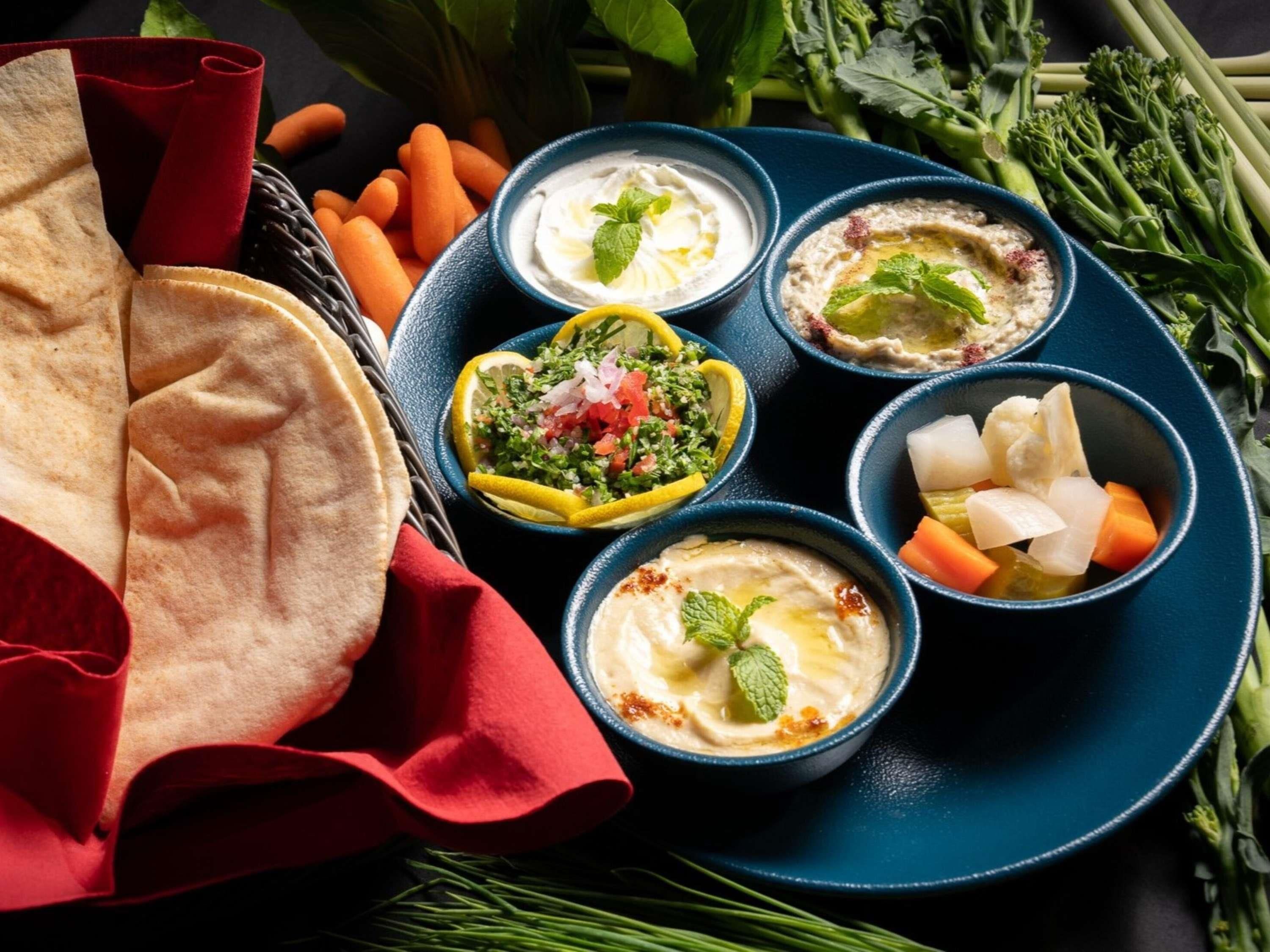 A plate with various dips and vegetables, a piece of flatbread, and a red napkin.