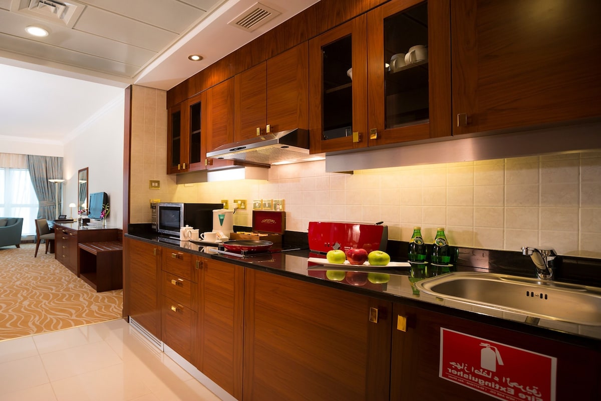 Habitación de hotel con kitchenette, comedor y sala de estar con sofá y sillones.