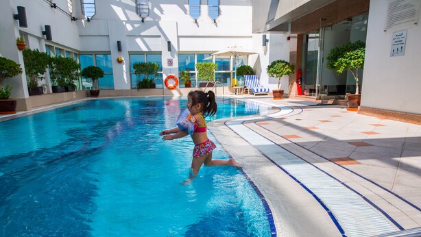 Un espace piscine où un enfant joue dans l’eau, entouré de plantes en pot et de chaises longues.
