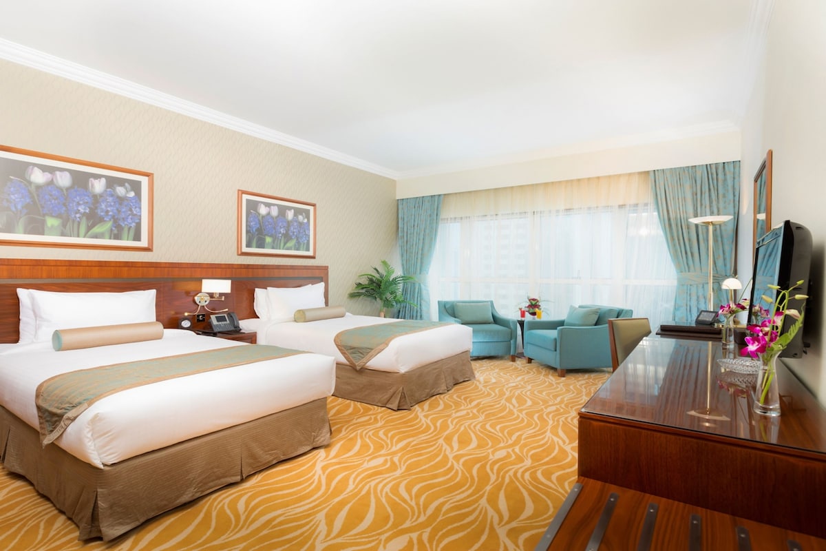 Habitación de hotel con dos camas, un sofá, un escritorio, un espejo y una ventana con cortinas.