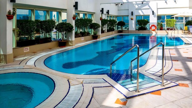 Una piscina interior con agua cristalina, rodeada de plantas en macetas y un solárium con baldosas.