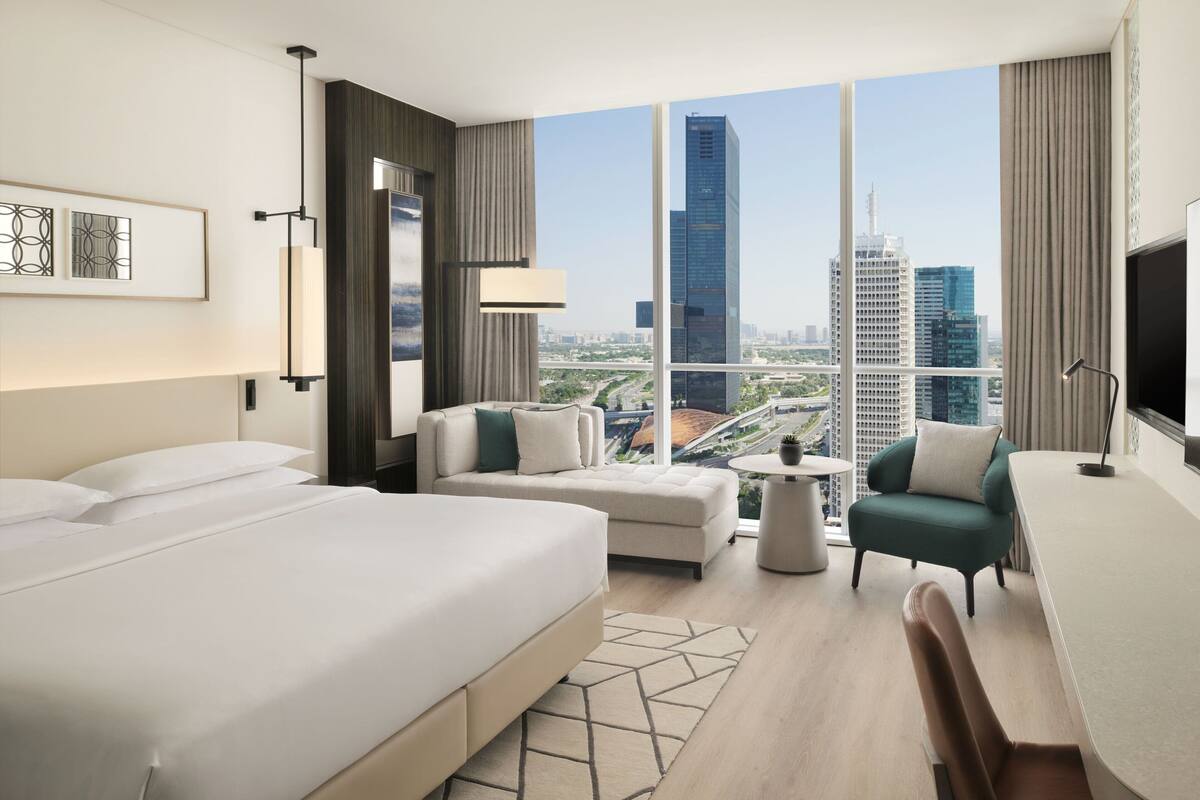 A modern hotel room with a large bed, a sofa, a desk, and a view of the cityscape.