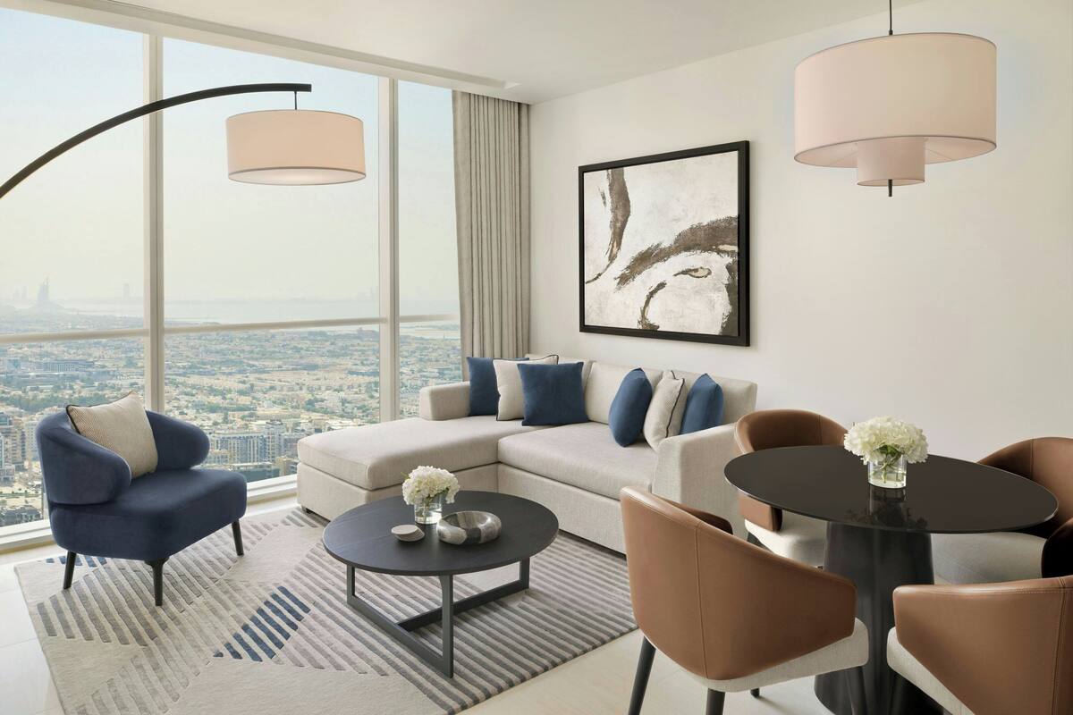 A modern living room with a sofa, armchairs, a coffee table, and a dining table. There is a large window offering a city view.