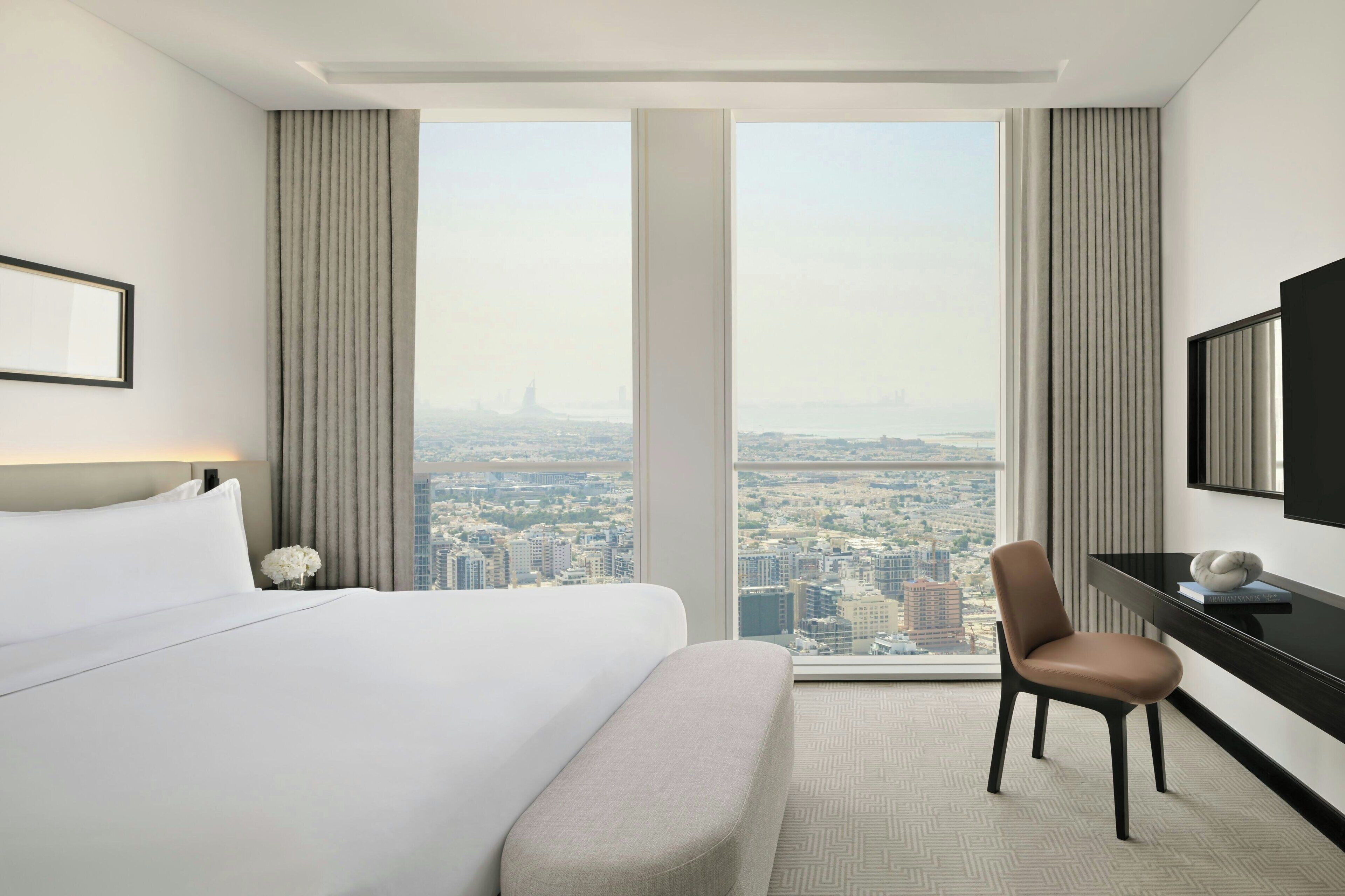 A hotel room with a large bed, a desk, a chair, and a city view.