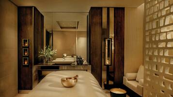 Ein moderner Spa-Raum mit einer großen Massageliege, einer Holz-Massagebowl, einem Waschbecken und einer Couch.