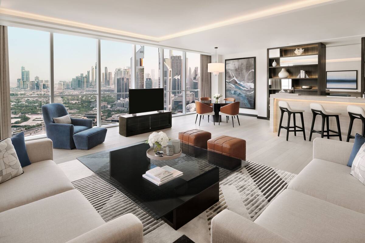 A modern living room with a large TV, comfortable seating, a dining area, and a kitchen bar.
