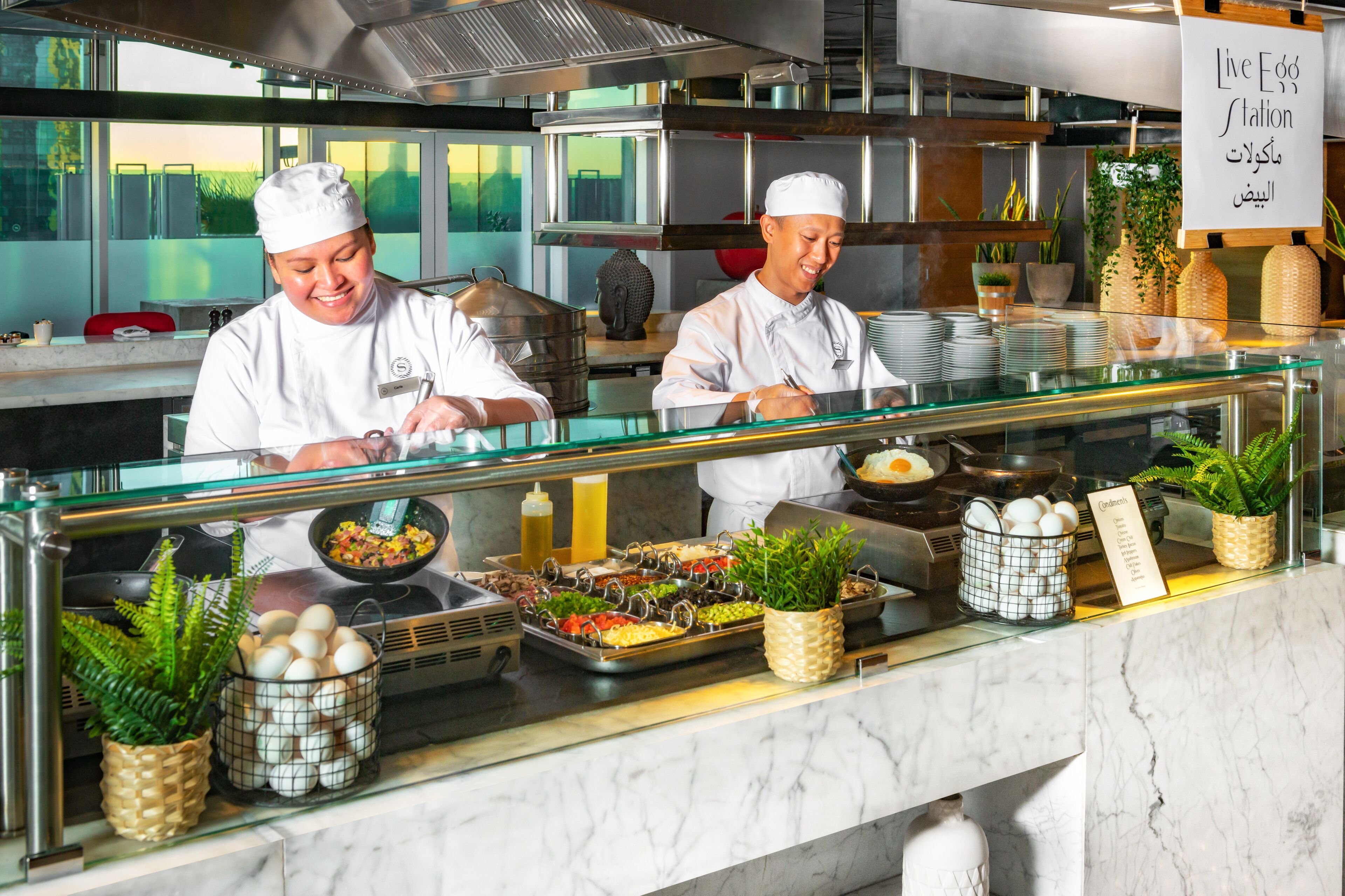 Een buffetopstelling met koks die eten bereiden, diverse gerechten en een bordje met de tekst 'Live Egg Station'.