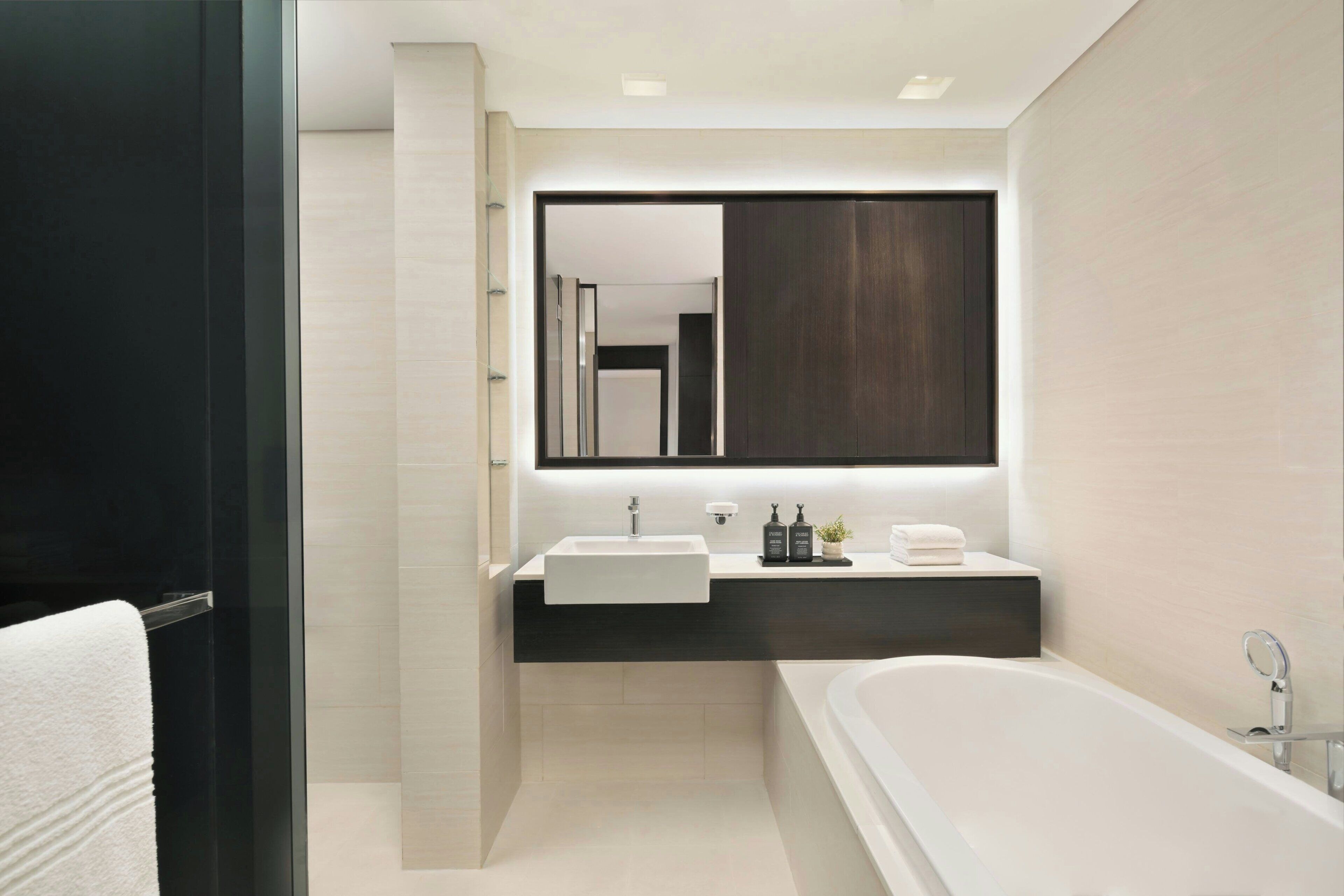 A modern bathroom with a large mirror, a white sink, a bathtub, and a dark vanity.