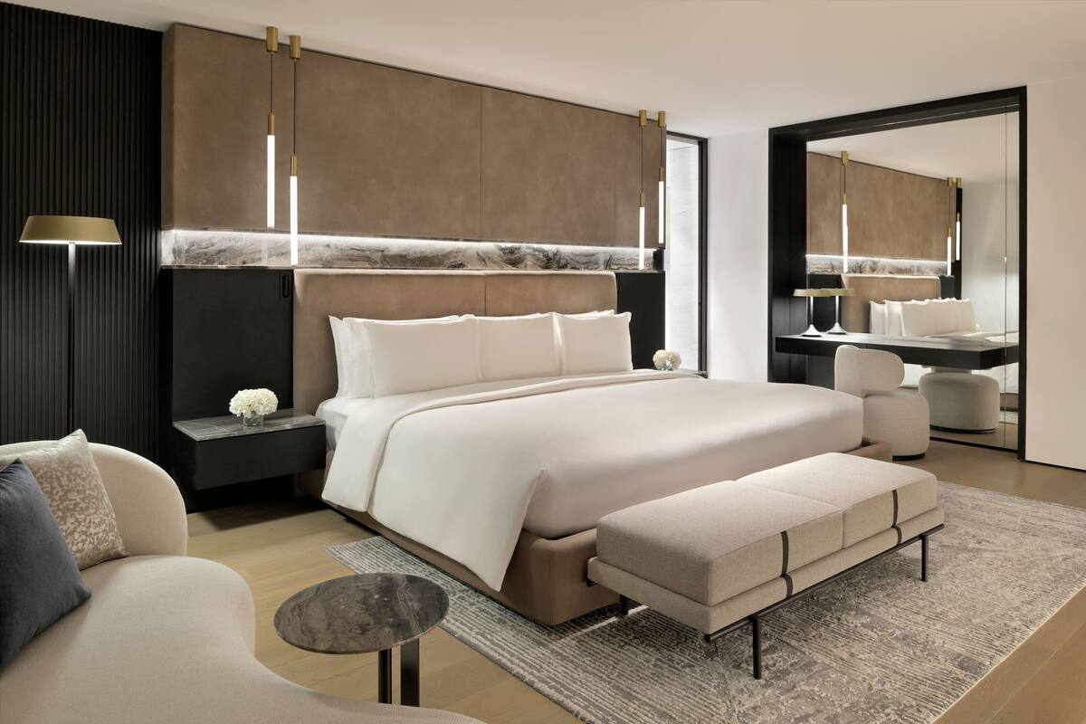 A modern bedroom with a large bed, bedside tables, a sofa, a small round table, and a mirror.