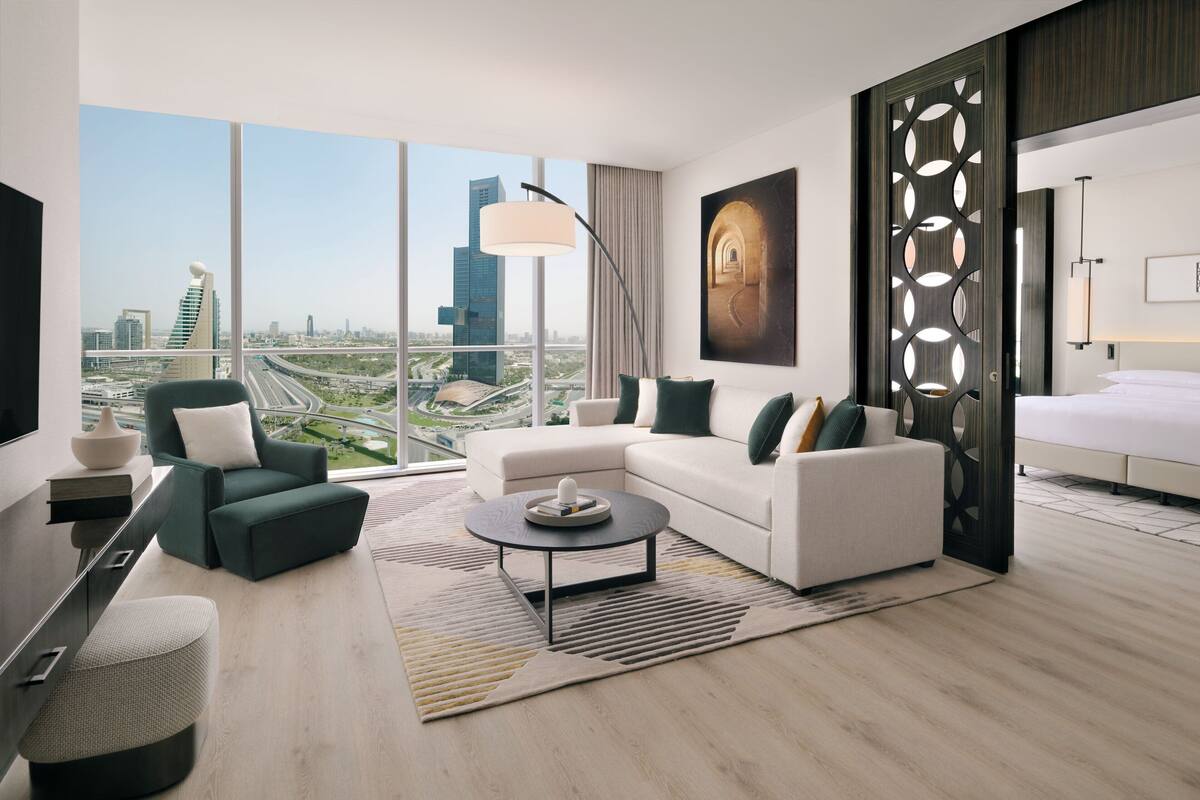 A modern hotel room with a city view, a sofa, a coffee table, and a bed.