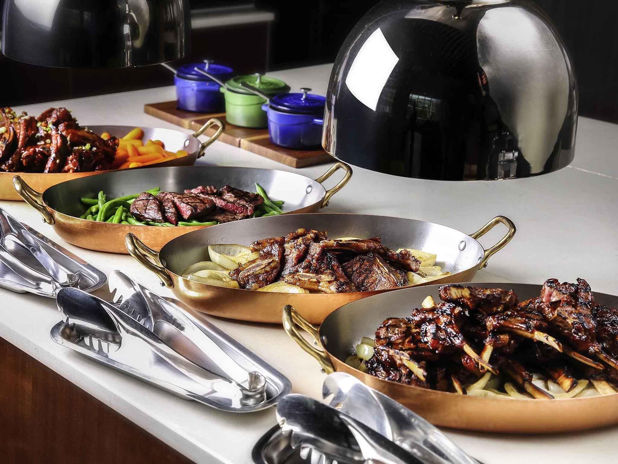 A buffet with various dishes including ribs, steaks, and vegetables.