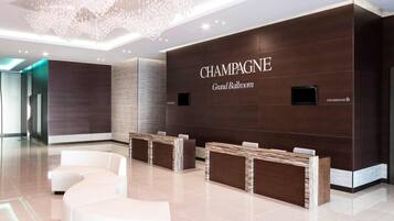 A modern reception area with a chandelier, a reception desk, and a sign reading 'CHAMPAGNE Grand Ballroom.'