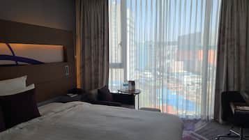 Habitación de hotel con una cama grande, un escritorio, una silla y vistas a una piscina y edificios.