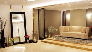 Una sala de estar moderna con un sofá color beige, un espejo grande y un jarrón decorativo con flores.
