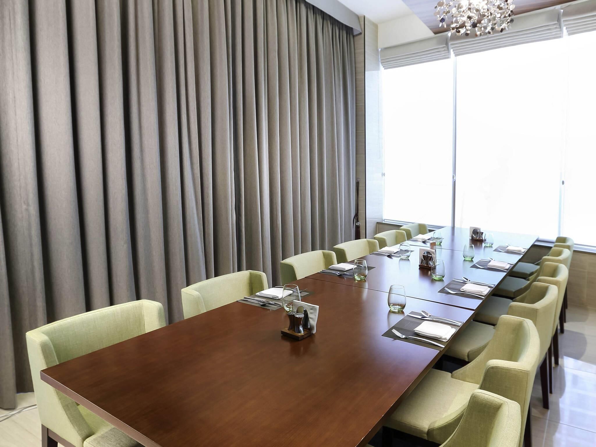 A conference room with a long table, multiple chairs, and a large window with curtains.