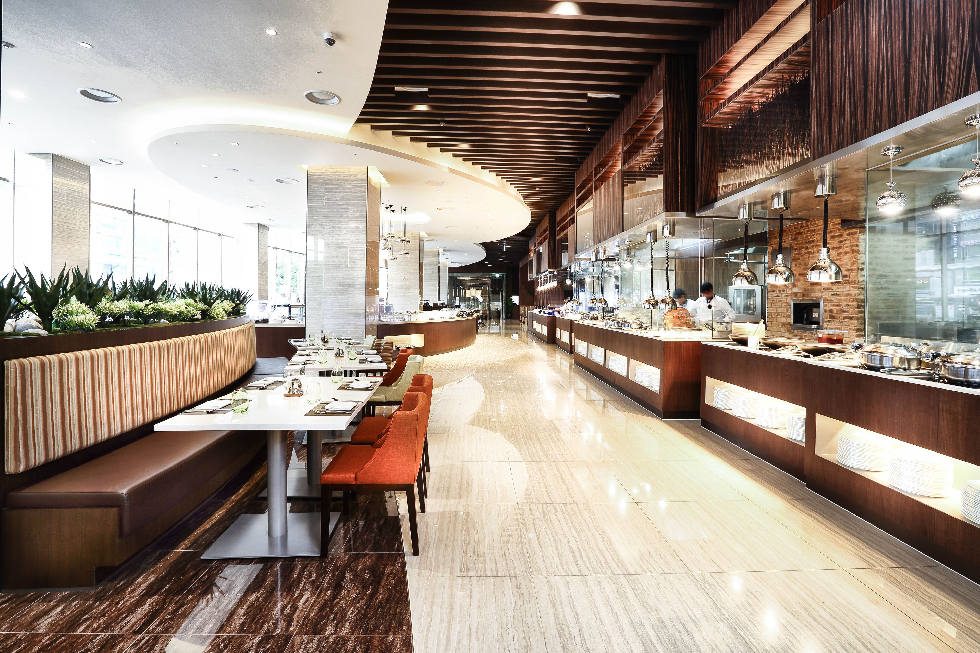 A modern restaurant with a long counter, seating area, and a kitchen visible through a glass partition.