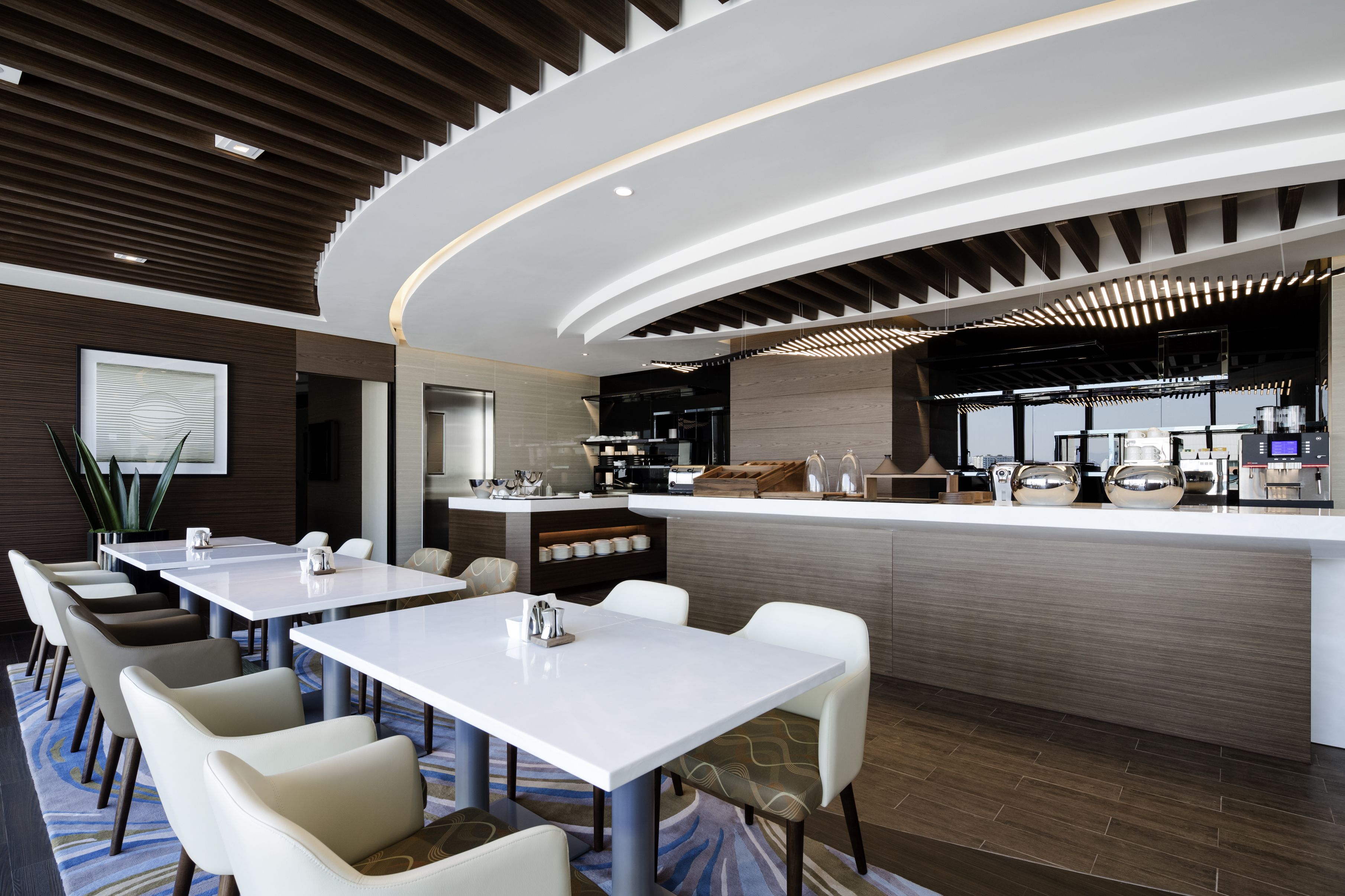 Un moderno vestíbulo de hotel con un mostrador de recepción curvo, zona de estar y una cocina visible al fondo.