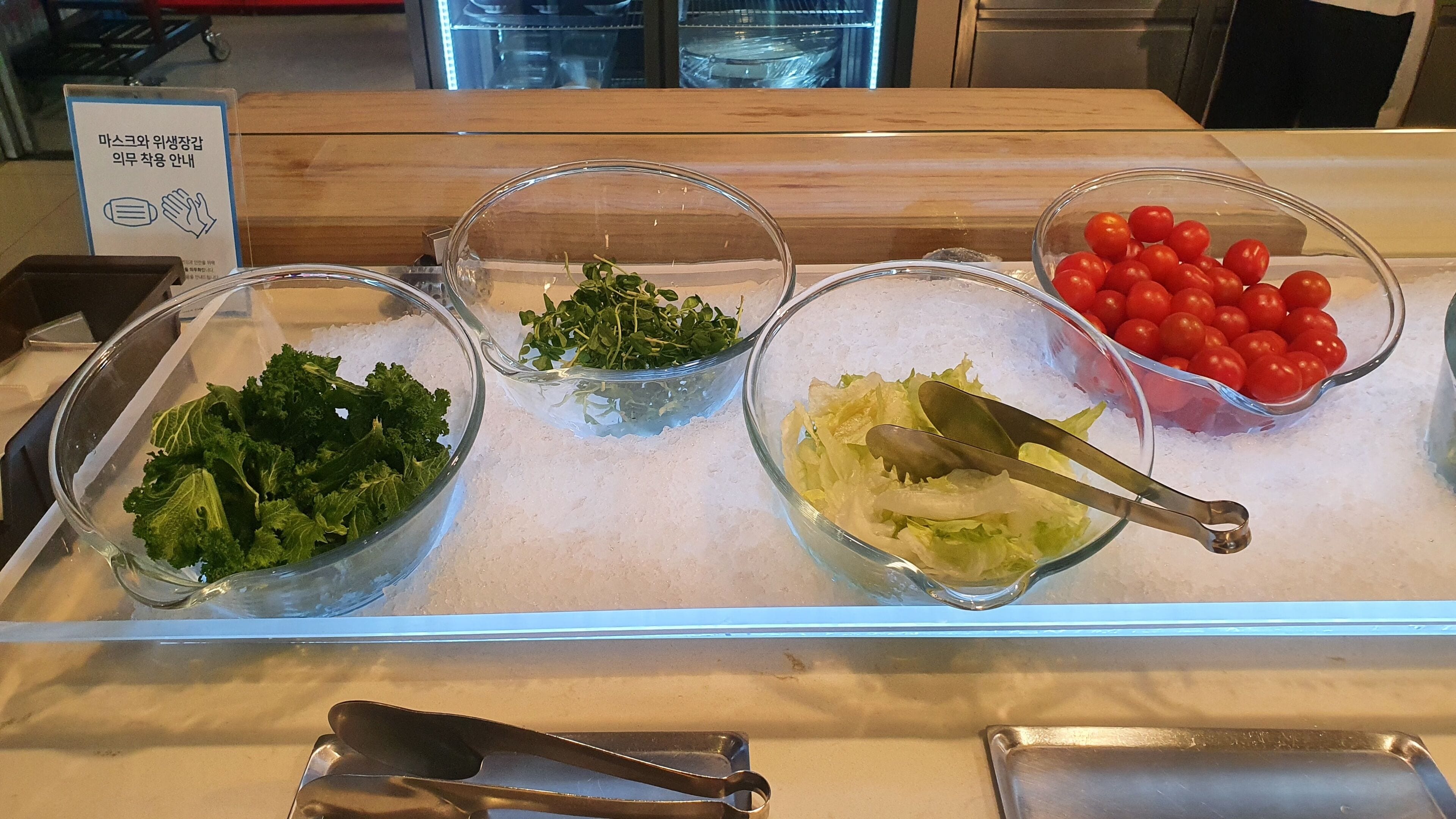 A salad bar with various fresh vegetables like lettuce, kale, and cherry tomatoes.