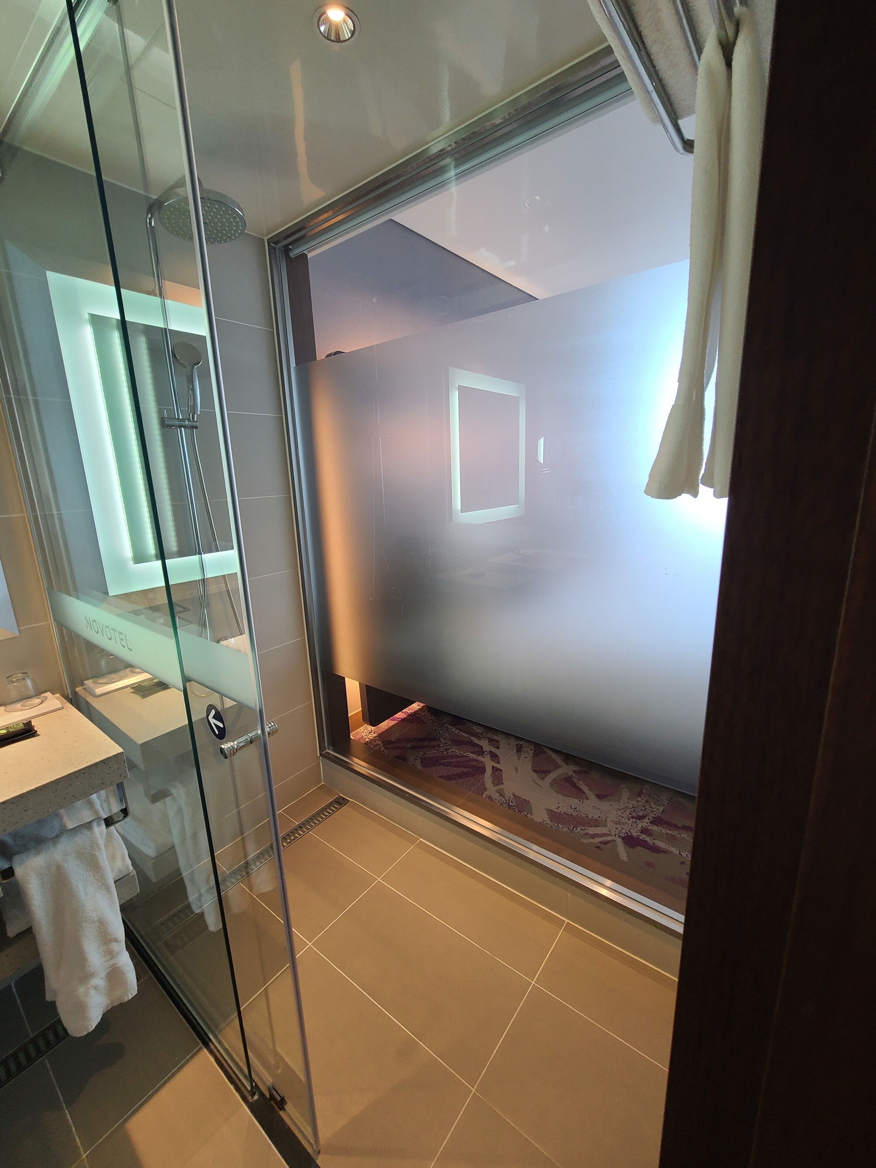 Un baño moderno con ducha de vidrio, tocador con espejo y perchero para toallas.