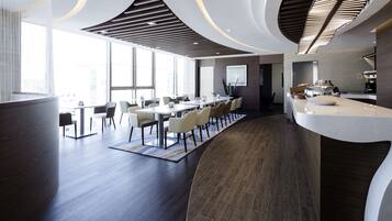 A modern conference room with a long table, chairs, and a kitchen area.