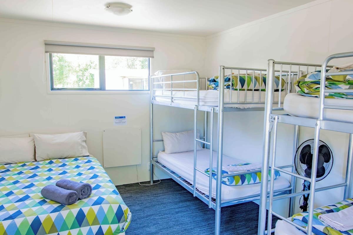 Habitación con literas, una ventana, una cama con colcha de estampado geométrico y un ventilador en la cama inferior.