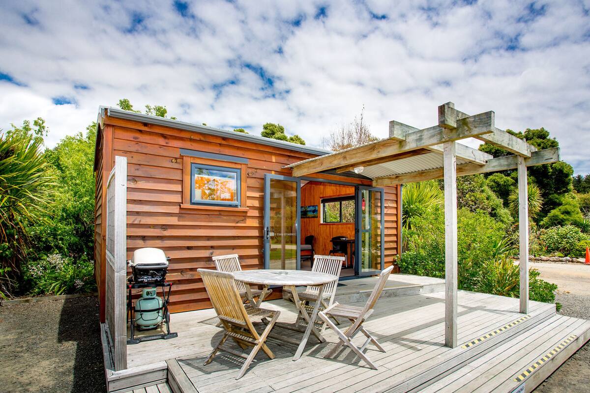 Una cabaña de madera con un patio, una mesa y sillas, y una pérgola.