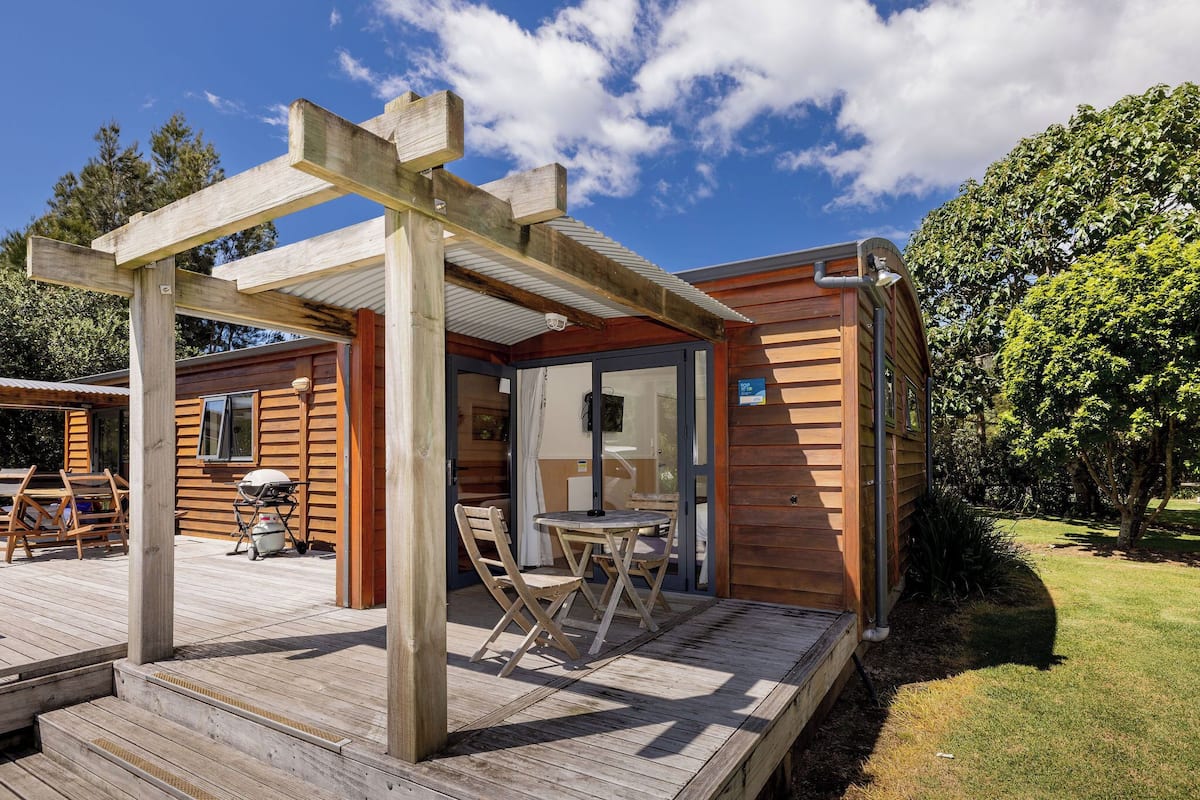 Una cabaña de madera con un porche, mobiliario exterior y una parrilla.