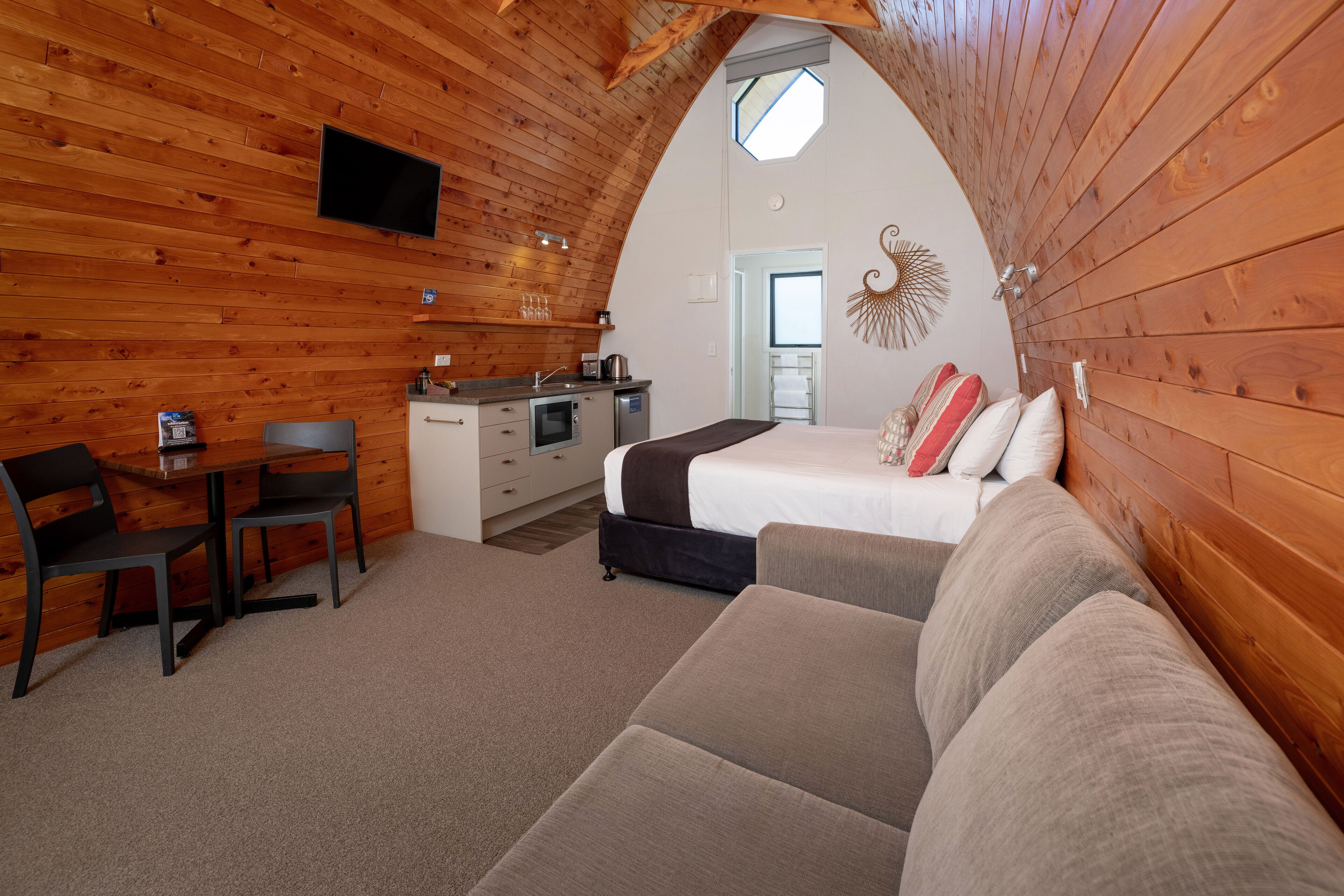 A cozy, wooden-paneled room with a kitchenette, a bed, and a sofa.