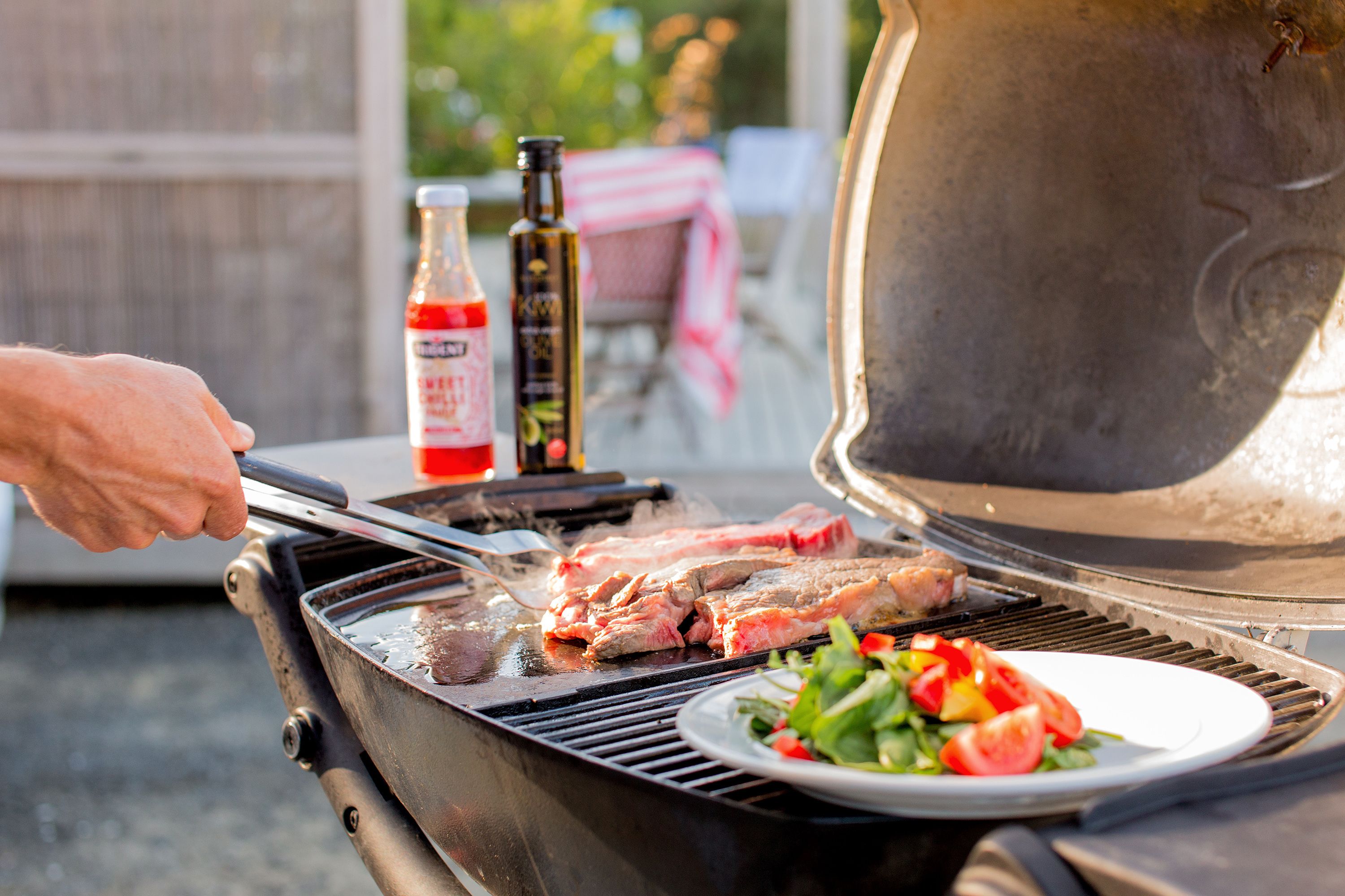 A barbecue grill with meat being cooked and a plate of salad nearby.