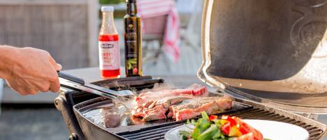 A barbecue grill with meat being cooked and a plate of salad nearby.