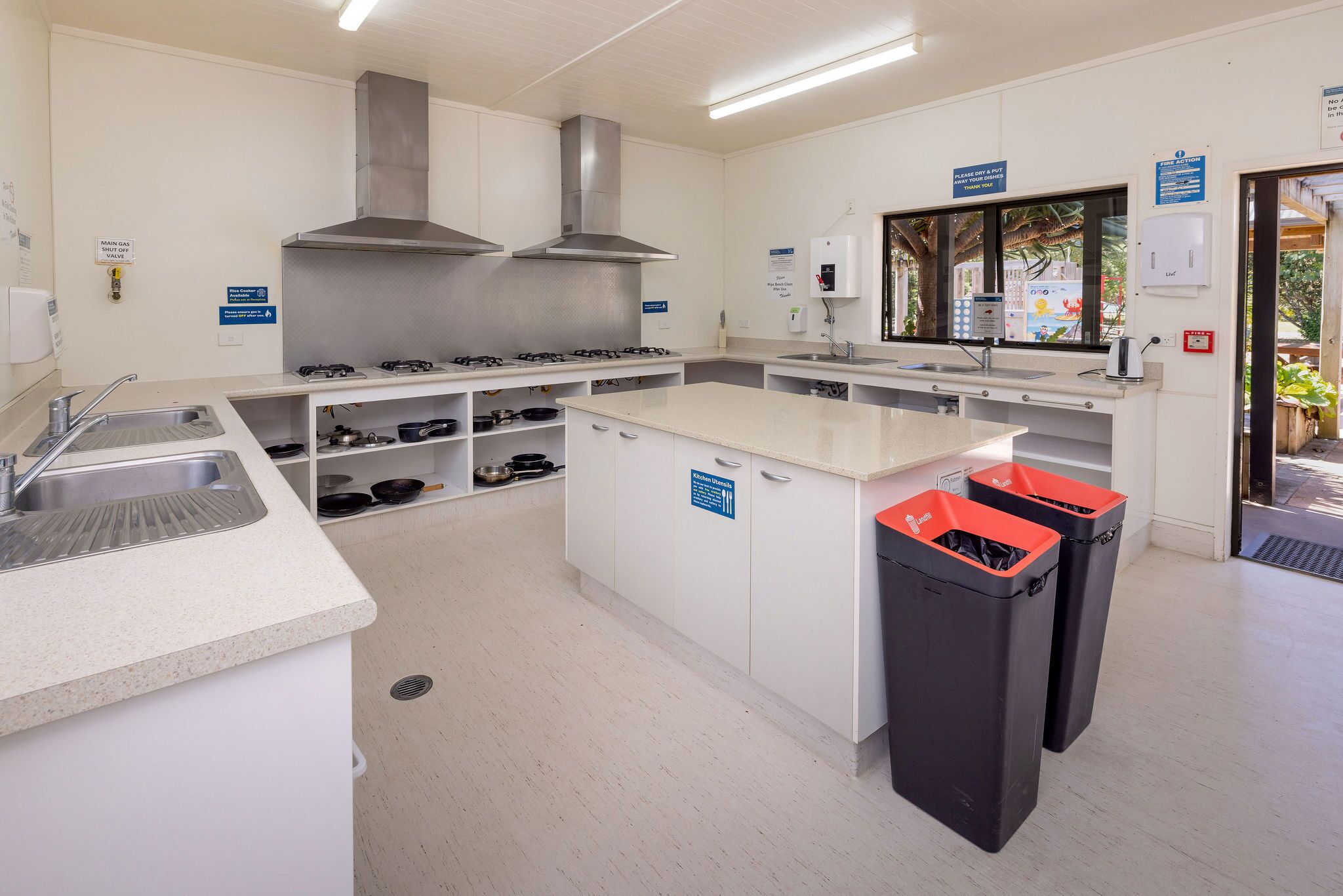 Una cocina moderna con electrodomésticos de acero inoxidable, un lavamanos y dos botes de basura.