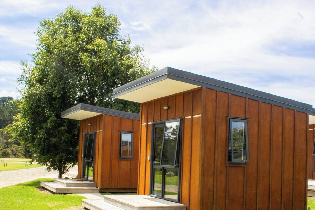 Una cabaña moderna de madera con ventanas amplias y un porche cubierto.
