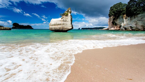 Ein Strand mit klarem türkisblauem Wasser, einer großen Felsformation und einem sandigen Ufer.