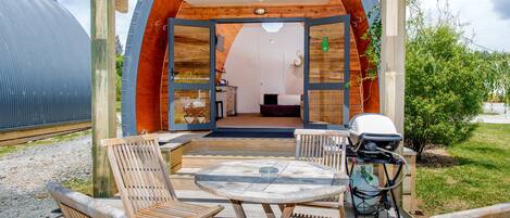 An outdoor wooden deck with a round table and four wooden chairs, a grill, and a water pump.