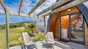 Eine Holzterrasse mit zwei Liegestühlen, einer Holzpergola und Blick auf ein modernes Haus mit Glastür.