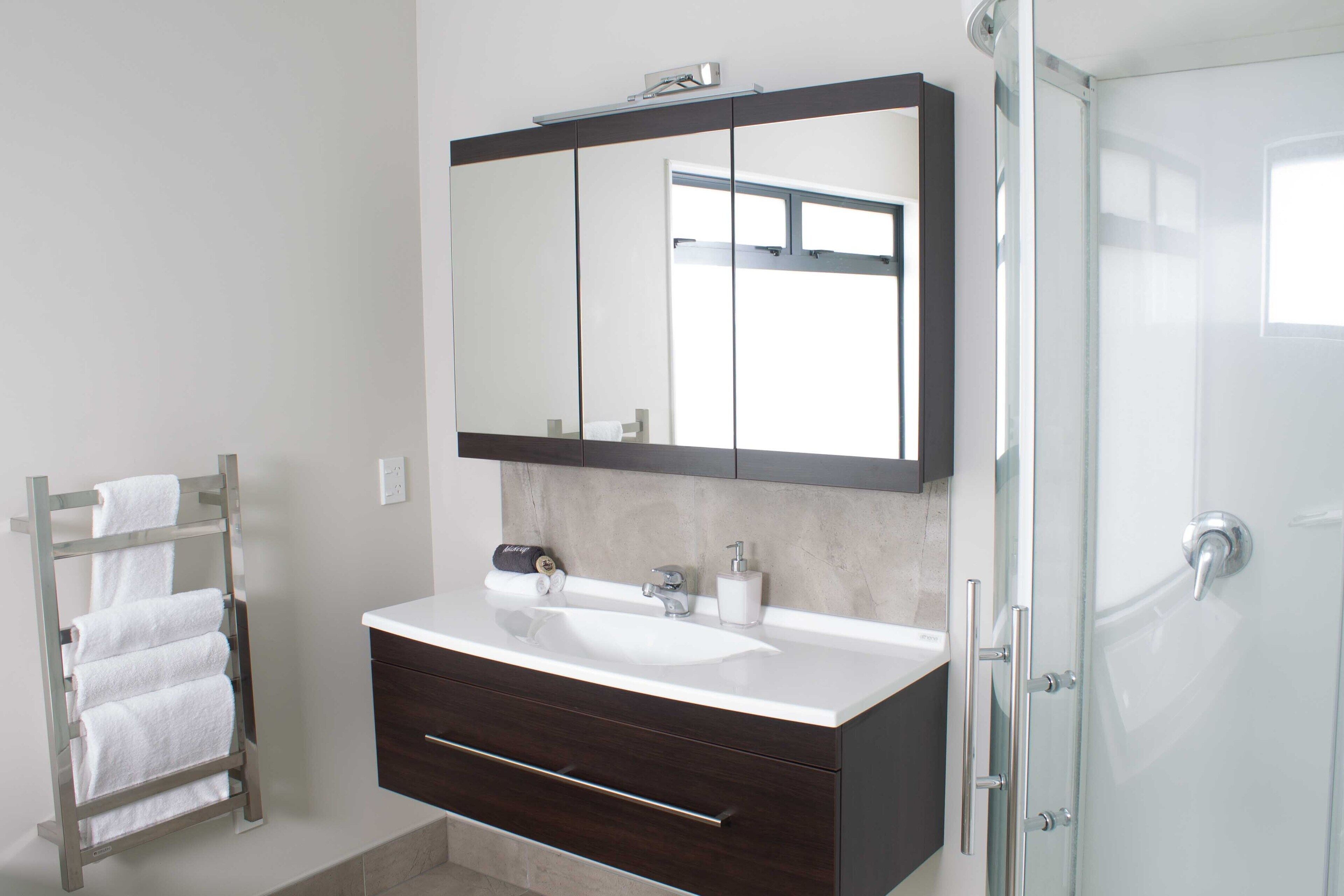 A modern bathroom with a large mirror, a white sink, dark wooden vanity, and a glass shower enclosure.